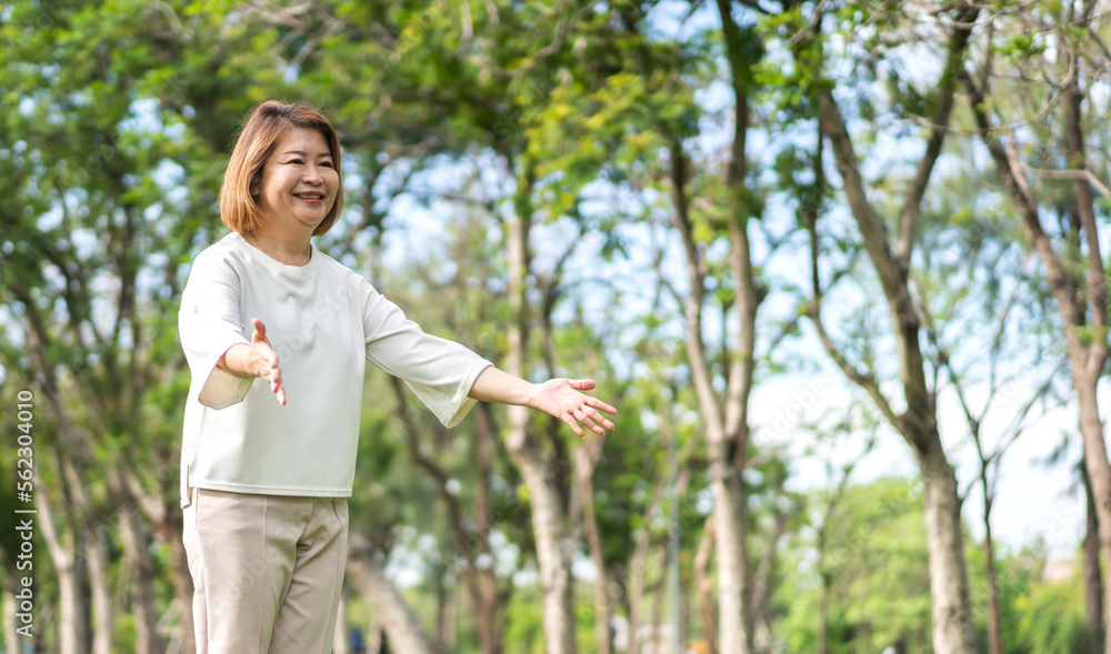 Portrait of happy senior old adult elderly asia women smiling standing and stretch her arms relax and enjoy with nature feeling breath fresh clean air in green park.Healthcare Portrait of happy senior old adult elderly asia women smiling standing and stretch her arms relax and enjoy with nature feeling breath fresh clean air in green park.Healthcare