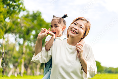 Portrait of happy love asian grandmother and asian little cute girl enjoy relax in summer park.Young girl with their laughing grandparents smiling together.Family and togetherness