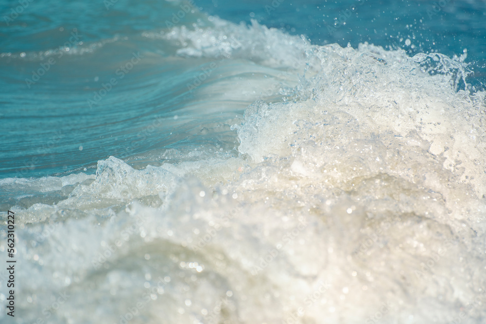 Close-up of the sea wave with the foam surging on the shore. View of sea water in soft focus. Background in a light blur on the theme of a serene summer vacation and relaxed vacation. Close-up of the sea wave with the foam surging on the shore. View of sea water in soft focus. Background in a light blur on the theme of a serene summer vacation and relaxed vacation.
