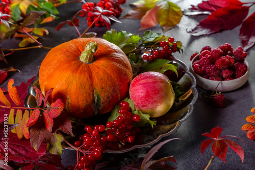 Pumpkin  apples and berries with autumn leaves on a textured table