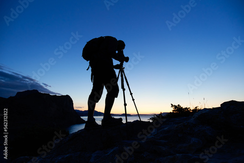 Silhouette of photographer on top of mountain at sunset background. Nature photographer in the action. Film analog photography