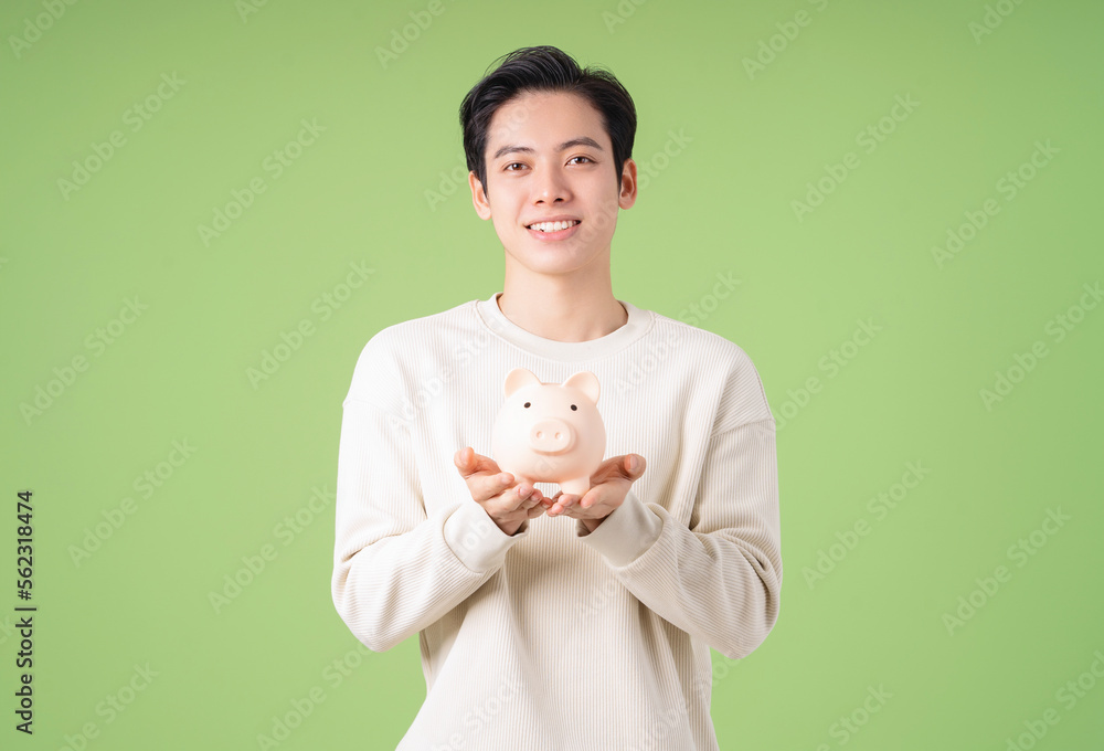 Image of young Asian man holding piggy bank on background Image of young Asian man holding piggy bank on background