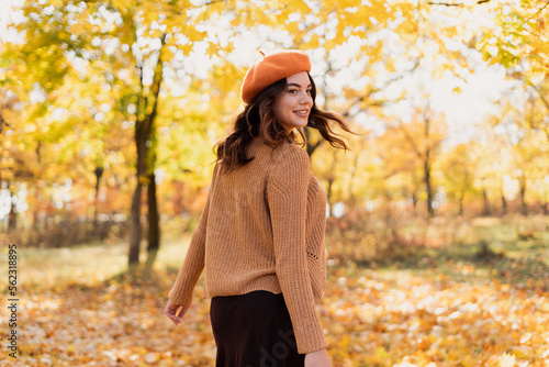 Happy young woman wearing warm sweater and beret in the park at sunny autumn day.