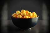 View of a bowl full of delicious, cheesy corn puffs in closeup on a black table. Generative AI