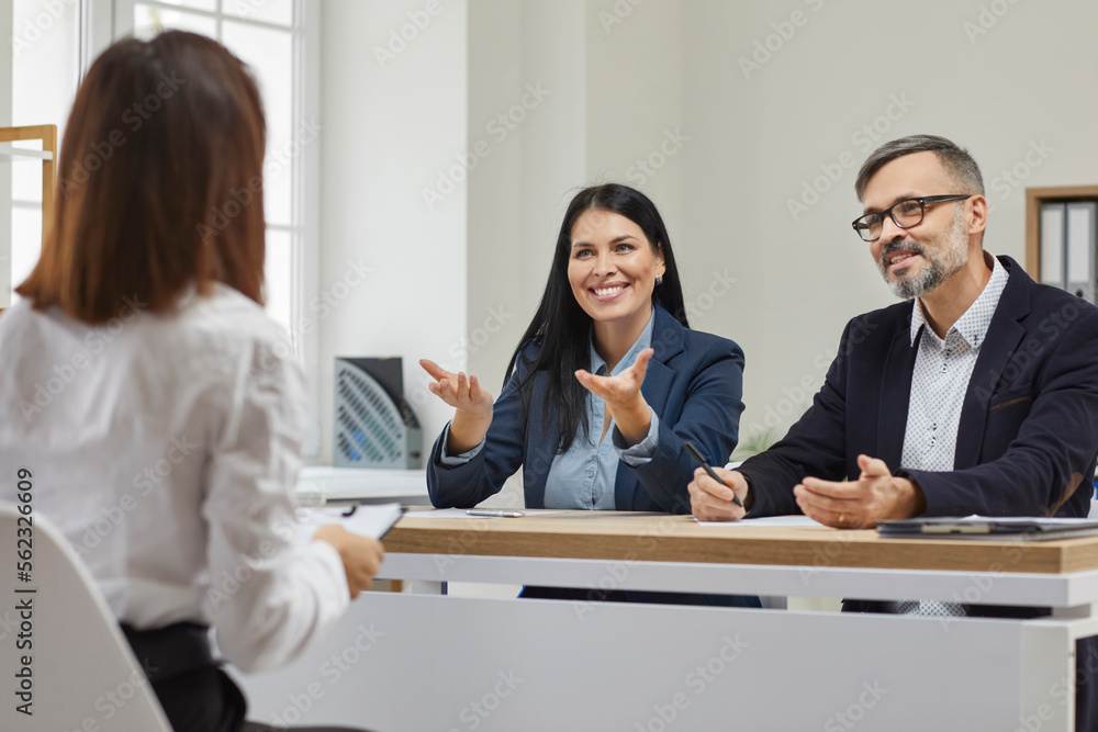 Smiling, friendly businessman with his beautiful colleague conducts interview for young girl for further cooperation and productive work in team. Positive atmosphere in spacious modern office. Smiling, friendly businessman with his beautiful colleague conducts interview for young girl for further cooperation and productive work in team. Positive atmosphere in spacious modern office.