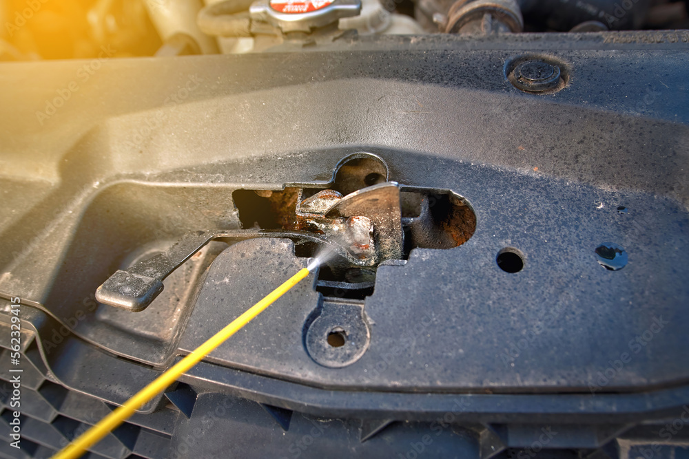 Lubricating car hood lock, spray and cleaning rusty hood lock of car, spraying grease, lubrication spray.