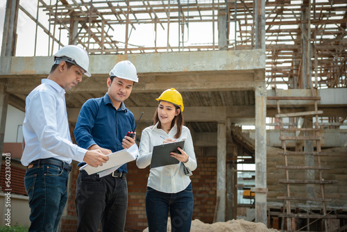 Asian Architector and engineers team with draft plan of building and tablet talking constructing site. Construction manager and engineer working on building site. © Thanumporn