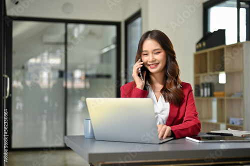 Professional Asian businesswoman looking business details on laptop screen while talking on the phone