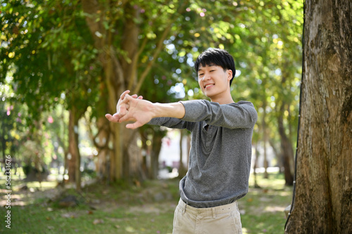 Happy young Asian man stretching his arms, relaxing in the beautiful park