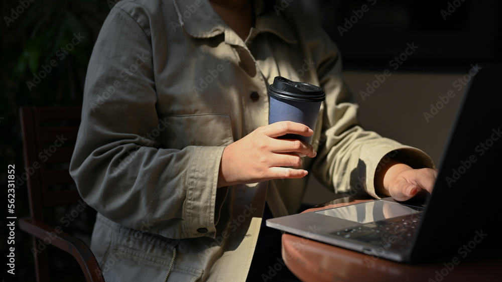 Female freelancer remote working at the coffee shop, sipping coffee while using her laptop