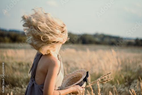 Close up blond woman hair blowing in summer wind concept photo. Side view photography with wheat field on blurred background. High quality picture for wallpaper, travel blog, magazine, article