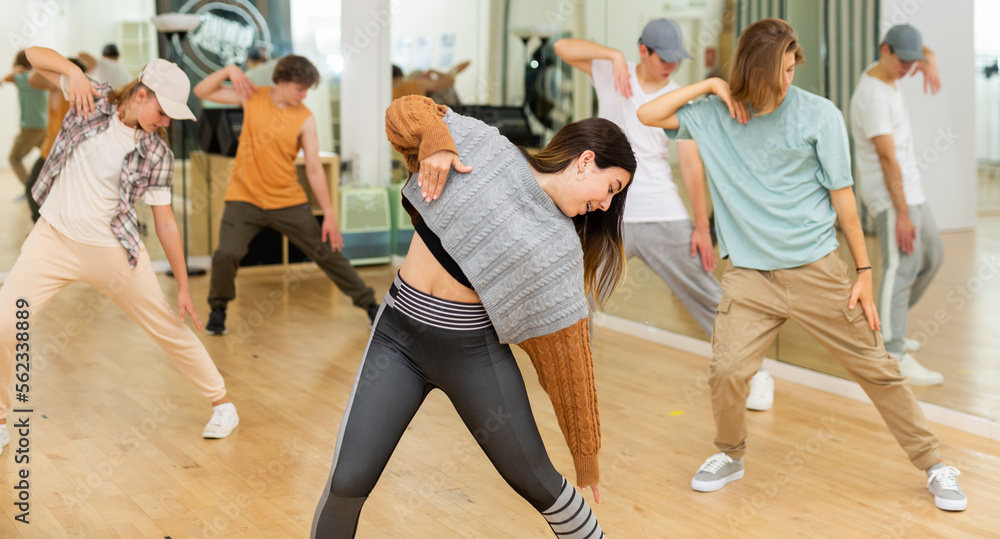 Portrait of expressive teen girl krump dancer in choreographic studio with dancing teenagers in background.