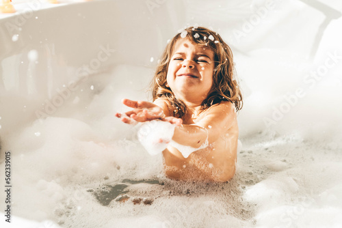 Little girl in bath playing with foam.