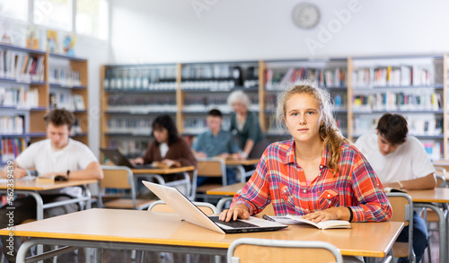 European fifteen-old-year schoolgirl, preparing for classes in the school library searches for information on a laptop and writes a abstract in a copybook