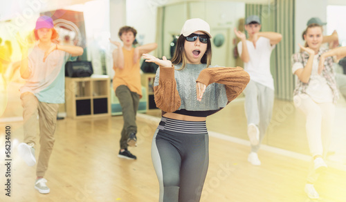 Fototapeta Naklejka Na Ścianę i Meble -  Portrait of expressive teen girl krump dancer in choreographic studio with dancing teenagers in background.