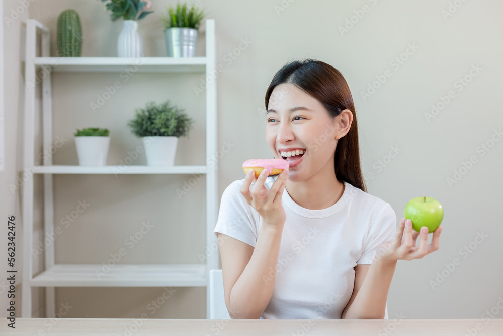 Beautiful asian female eating donut and holding apple choosing healthy eat. healthy food choices. Girl keep their diet. Diet healthy food concept. Beautiful asian female eating donut and holding apple choosing healthy eat. healthy food choices. Girl keep their diet. Diet healthy food concept.