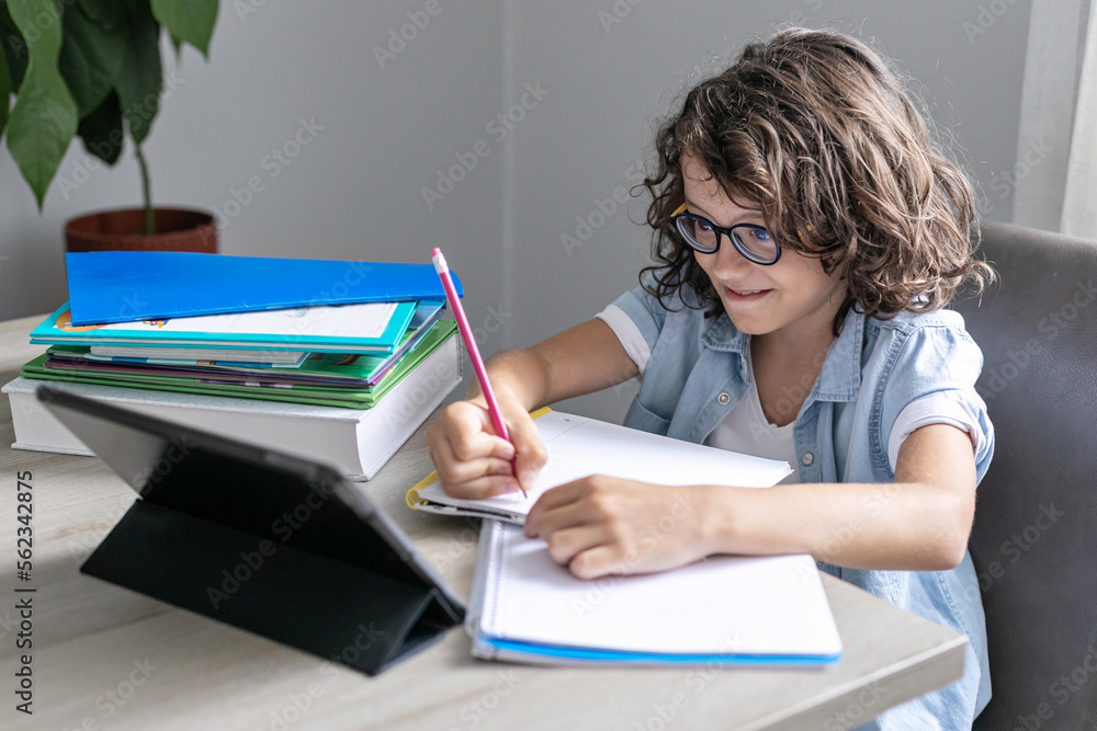 Little adorable school boy with curly hair and eyeglasses, studying remote online from home. Concentrated kid using digital tablet, learning at video class. Little adorable school boy with curly hair and eyeglasses, studying remote online from home. Concentrated kid using digital tablet, learning at video class.