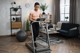 Young attractive sporty african american woman in sportswear having morning workout at modern light apartment. Healthy athletic female jogging while training at treadmill.