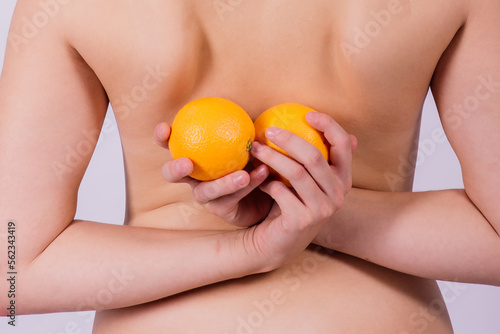 Slim woman is holding orange. Perfect female back without cellulite.