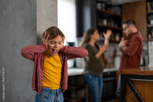 Fotografia, Obraz Depressed little girl covering her ears and screaming while her mother and father are having a serious conflict in the background, blaming each other