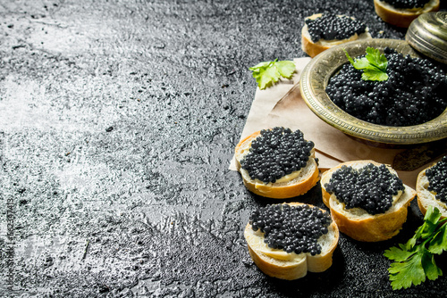 Sandwiches with black caviar and caviar in a bowl on paper with parsley.