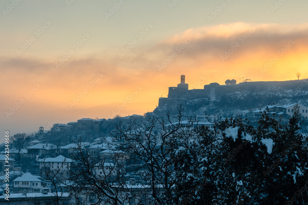 View of the citadel of Gjirokastër (Gjorikaster), Albania in the golden morning light, by sunrise. Winter, snow landscape with roofes covered with snow.