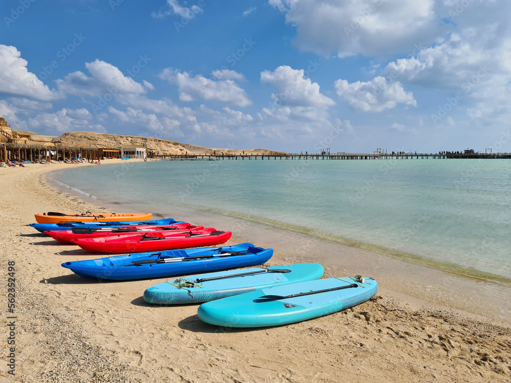 Colored windsurfing boards and canoes lie on the sea beach. Active recreation.