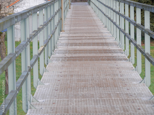 Perspektive Sicht auf eine Fußgängerbrücke mit Stahlgeländer und Gitterrost zur Überquerung einer Überschwämmungsfläche © Brightlight