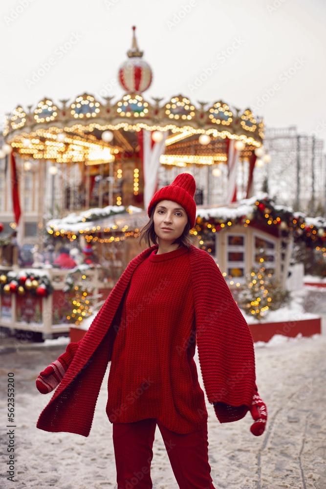 woman in a red warm sweater and hat in winter stands on red square in Moscow against the background of a carousel on Christmas day.