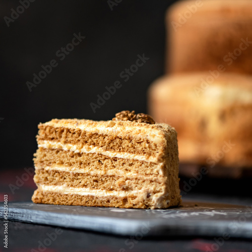 Piece of honey cake decorated with walnuts on plank. Cross-sectional view. Eastern European cuisine. Dark background. Close-up. 