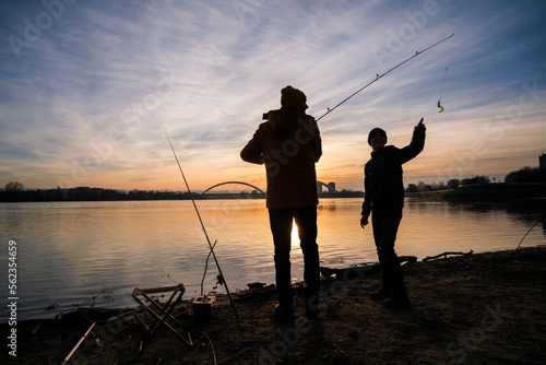 Father and son are fishing on winter day. River fishing. Teenage boy is learning to fish.