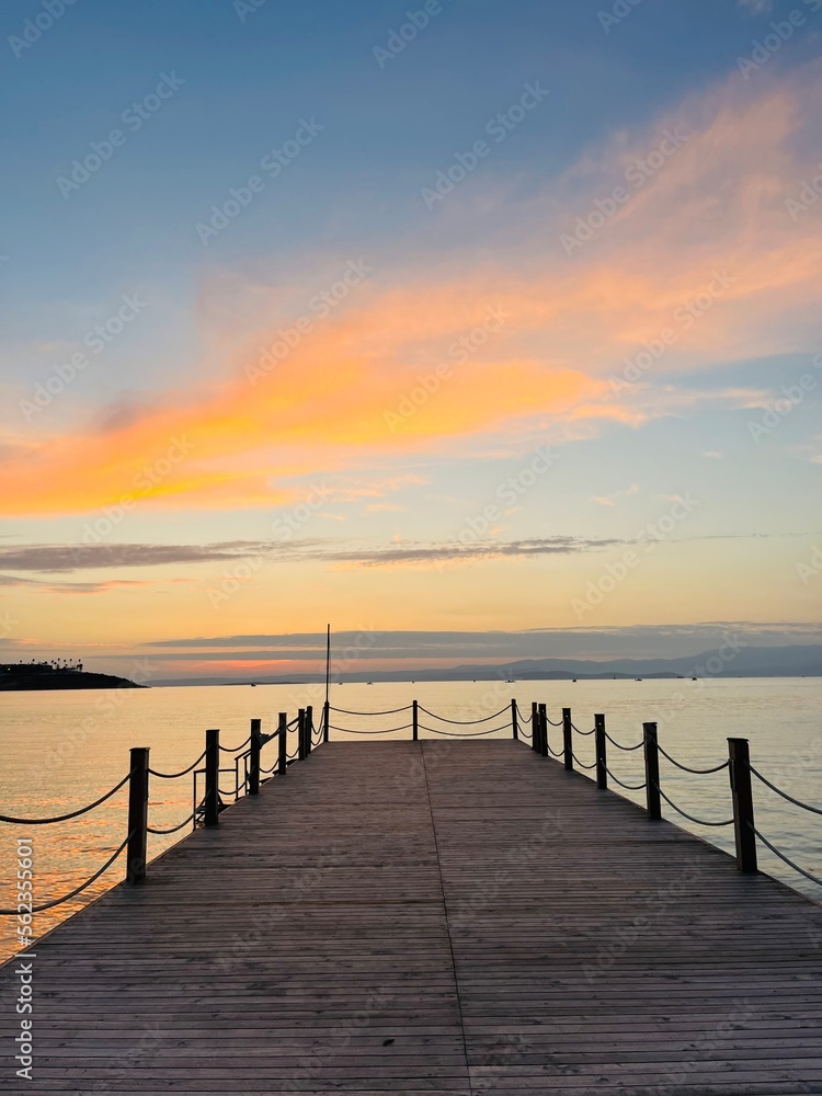 Empty wooden pier at the sea, sunset time, orange and purple clouds