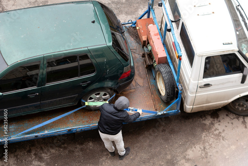 The tow truck driver fixes the broken car on the tow truck.	