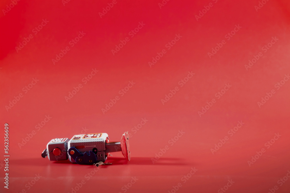 A retro tin toy robot, fallen while walking, lying on the floor over a red backdrop (lost mechanical power charge).
A retro tin toy robot, fallen while walking, lying on the floor over a red backdrop (lost mechanical power charge).