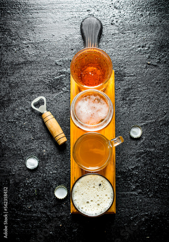 Various glasses of beer on a wooden cutting Board with opener.