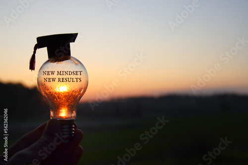 Hand holding light bulb with the text new mindset in front of the bright sun