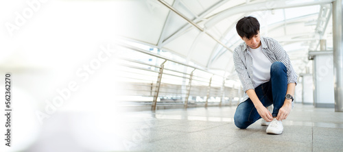 Asian young man sitting on the ground and tie a shoelaces with copyspace. A Man traveling in the city or downtown and tying a shoelace.