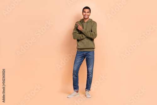 Full length photo of attractive joyful man wear khaki clothes arm direct empty space positive feedback isolated on beige color background