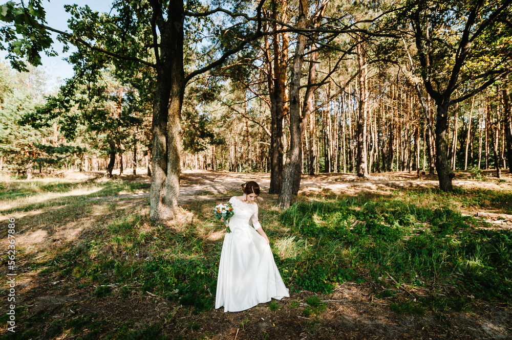 Young beautiful girl in elegant dress is standing and holding hand bouquet of white flowers and greens with ribbon at nature. The bride holds a wedding bouquet outdoors. Young beautiful girl in elegant dress is standing and holding hand bouquet of white flowers and greens with ribbon at nature. The bride holds a wedding bouquet outdoors.