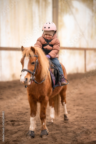 Little Child Riding Lesson. Three-year-old girl rides a pony and does exercises © dtatiana
