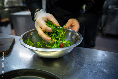 Chef hand mixing a vegetable salad in stainless steel bowl on kitchen