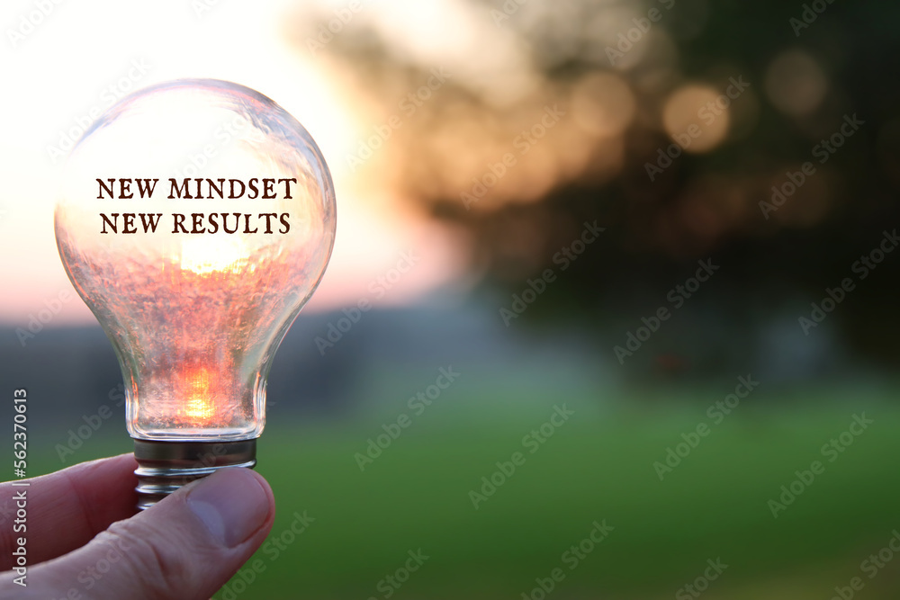 Hand holding light bulb with the text new mindset in front of the bright sun - obrazy, fototapety, plakaty 