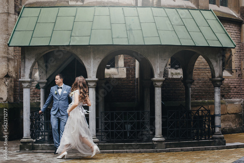 Stylish happy bride and groom walking on background of church . Provence wedding. Beautiful emotional wedding couple in european city.