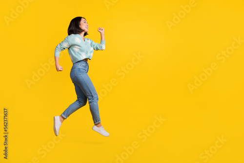 Full size side profile photo of cheerful girlish woman dressed blue pullover running look empty space isolated on yellow color background