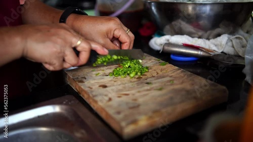 A person chopping spring onion on a wooden cutting board