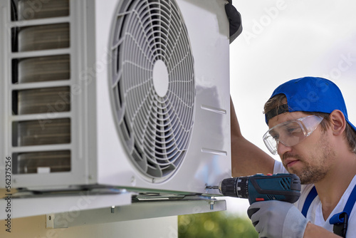 Work of the master installer of the air conditioner on the facade of the building using a screwdriver. An experienced craftsman fixes the air conditioner unit to the wall with automatic screwdriver
