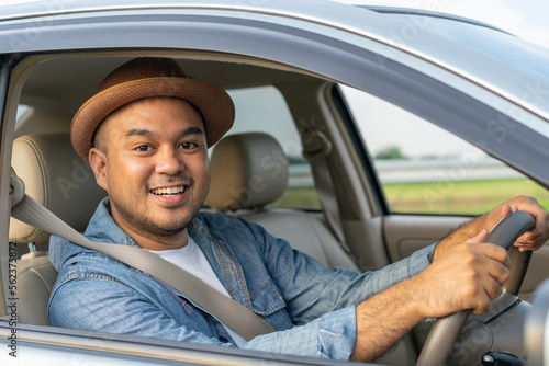 Happy male driver smiling while sitting in a car with open front window. Young asian man smile and looking through window. View of a Young man driving his car to travel on his holiday vacation time.