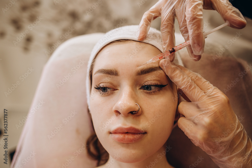 Naklejka premium Portrait of young Caucasian woman getting botox cosmetic injection in forehead. Beautiful woman gets botox injection in her face.