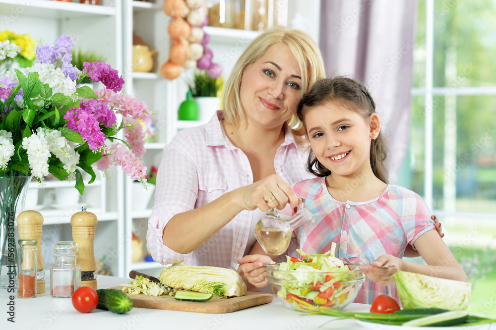 Cute little girl with her mother cooking together at kitchen table Cute little girl with her mother cooking together at kitchen table