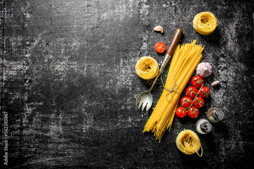 Raw spaghetti and tagliatelle with cherry tomatoes, garlic and a ladle.